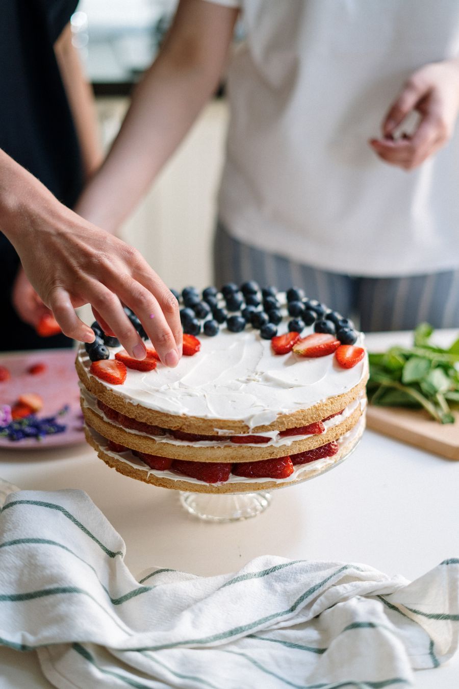 A baker arranging fresh berries on top of a finished cake.