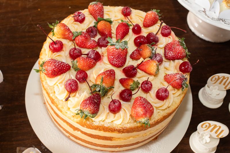 A layered cake topped with fresh strawberries and cherries.